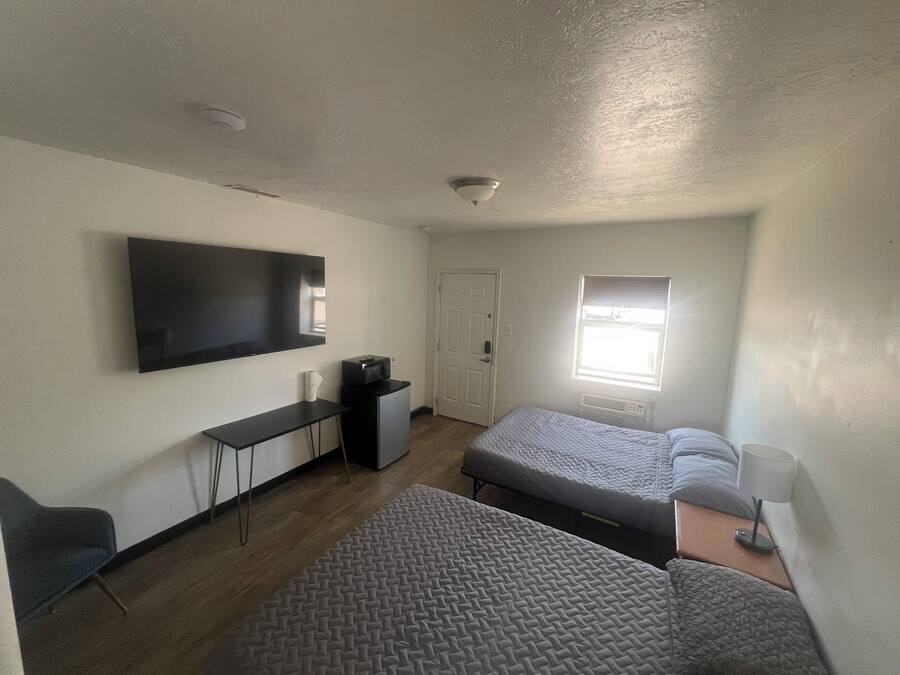A compact room with a flat-screen TV, a desk, a chair, two beds, a window, and a ceiling light.