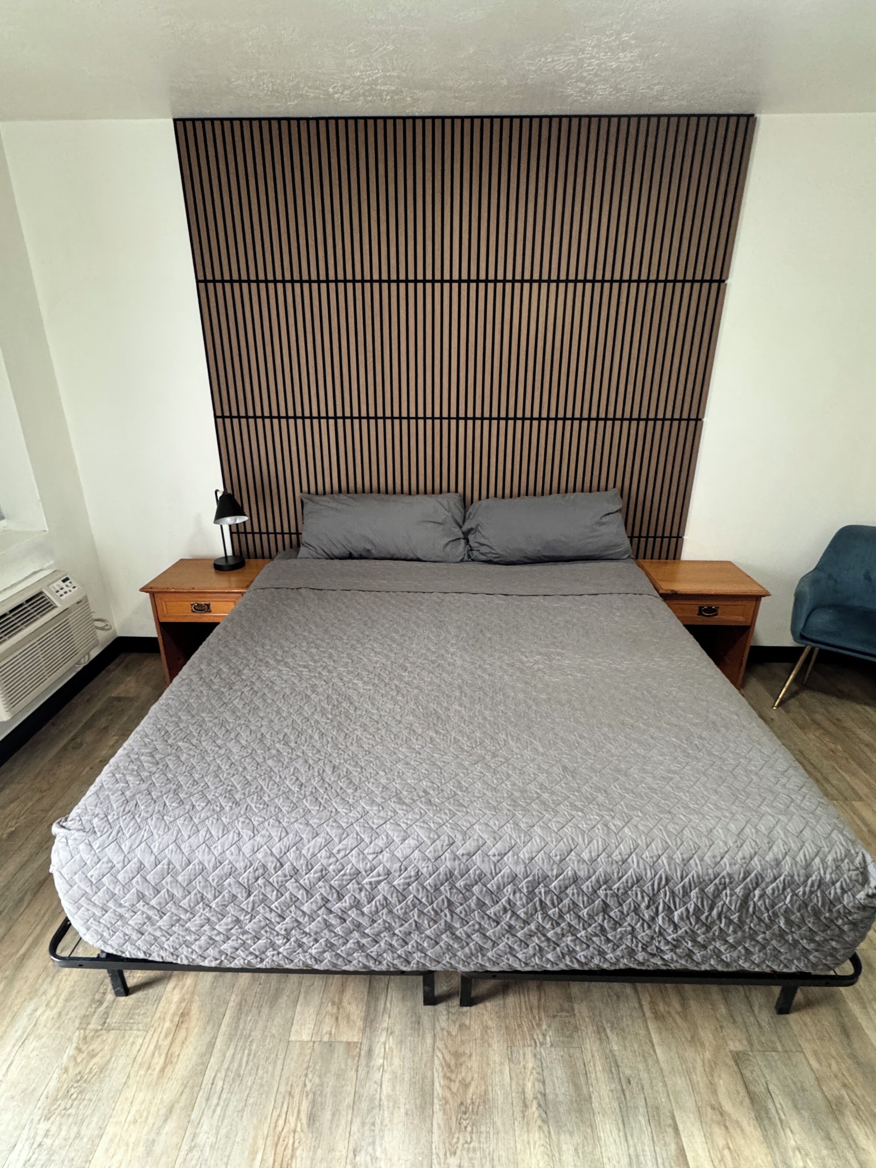 A modern bedroom with a large bed, a wooden headboard, two bedside tables, and a blue chair.