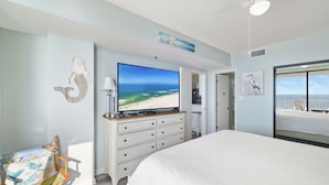 Een slaapkamer met een groot bed, een televisie, een dressoir en uitzicht op het strand.