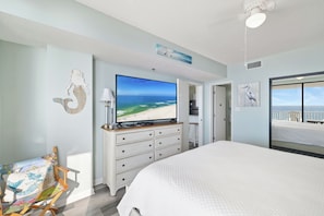 Quarto com cama grande, televisão, penteadeira e vista para a praia.