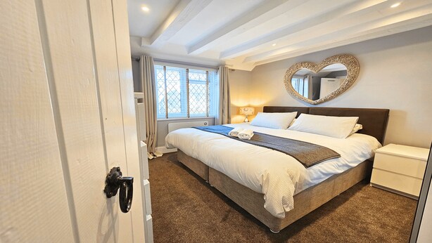 A bedroom with a bed, a nightstand, a heart-shaped mirror, and a window with curtains.