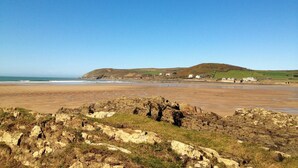 A coastal landscape with rocky terrain, a sandy beach, and a hill in the background.