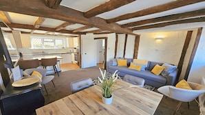 A cozy living area with a wooden table, a sofa with yellow cushions, and a dining area with chairs.