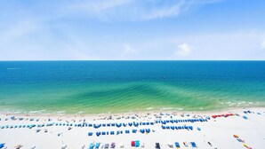 Une plage bordée de rangées de parasols bleus et rouges, avec du sable blanc et l’océan.