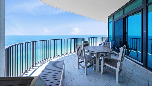 Un balcon avec vue sur l’océan, une table ronde avec des chaises et une porte vitrée.