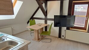 A compact kitchen with a dining area, a TV mounted on the wall, and a window with a view of buildings. - Cozy vacation apartment in a historic building (Harztor)