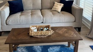A living room with a beige sofa, dark blue pillows, a wooden coffee table, and a woven wall decoration.