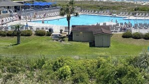 A pool area with lounge chairs and a small building, overlooking a beach and ocean.