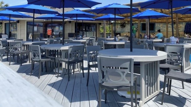 An outdoor seating area with round tables and blue umbrellas, surrounded by a wooden deck.