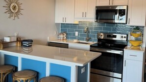 A modern kitchen with white cabinets, a central island with stools, stainless steel appliances, and a decorative sunburst wall clock.