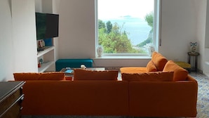 A living room with a large window offering a view of the sea and greenery. - Cozy Caprese house with breathtaking views of the island (Capri)