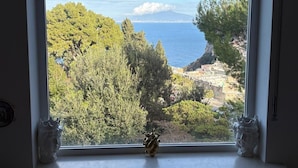 A room with a large window overlooking a coastal landscape, including trees, a cliff, and a view of the sea. - Cozy Caprese house with breathtaking views of the island (Capri)