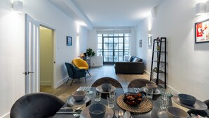 Un espace de repas moderne avec une table dressée pour quatre personnes, un canapé et une chaise en arrière-plan.