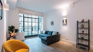 Un salon moderne avec un canapé gris, un fauteuil jaune et une étagère noire, le tout placé devant un mur blanc.