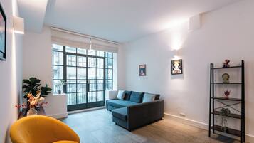 A modern living room with a grey sofa, a yellow armchair, and a black shelving unit against a white wall.
