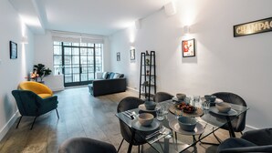 Un espace repas moderne avec une table en verre, des chaises noires et un canapé en arrière-plan.