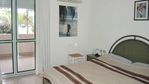 A bedroom with a bed, a nightstand, a chair, a picture on the wall, and an air conditioning unit. - Spacious Apartment With Terrace and Pool in Bibione (San Michele al Tagliamento)
