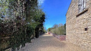 A gravel path leading to a stone building with a brick wall and a wooden fence.