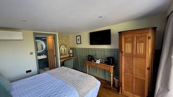 Un dormitorio con cama, un armario de madera, un escritorio con espejo, televisión y un baño visible a través de una puerta abierta.