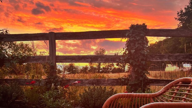 A wicker table and chairs on an outdoor patio with a view of a sunset over a body of water.