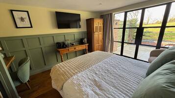 Une chambre dotée d’un grand lit, d’une table de chevet en bois, d’un téléviseur fixé au mur et d’une fenêtre donnant sur l’extérieur.