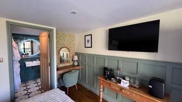 A hotel room with a bed, a desk with a computer, a TV, a bathroom with a mirror, and a shower.