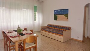 A dining area with a wooden table and chairs, a sofa with a colorful cushion, and a painting on the wall. - City Center Apartment Walk to sea (San Michele al Tagliamento)