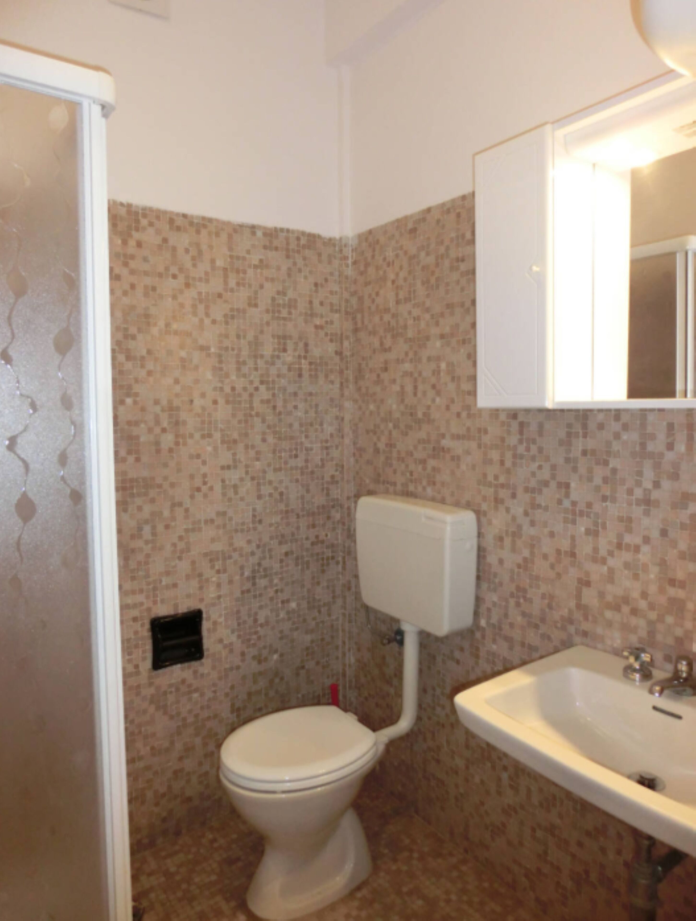A bathroom with a toilet, sink, and tiled walls.