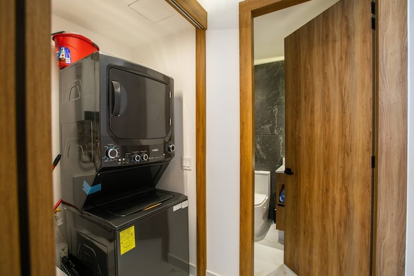 Una kitchenette compacta con microondas, un refrigerador pequeño y un cubo rojo.