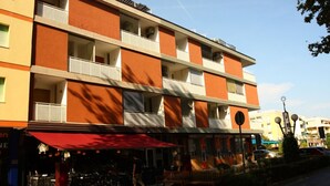 A multi-story hotel with balconies, outdoor seating, and a red awning. - Beachside Flat With Balcony (San Michele al Tagliamento)