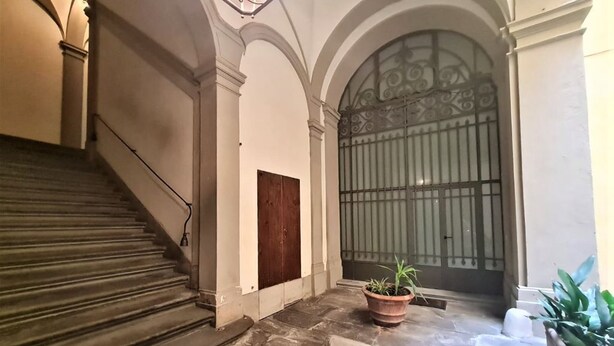 A grand staircase leading to a door with a metal gate, a potted plant, and a stone floor. - ELEGANT APARTMENT IN THE HEART OF FLORENCE, PIAZZA SIGNORIA (Firenze)