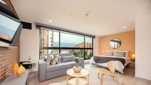 A modern bedroom with a large window, a bed, a sofa, and a small table.