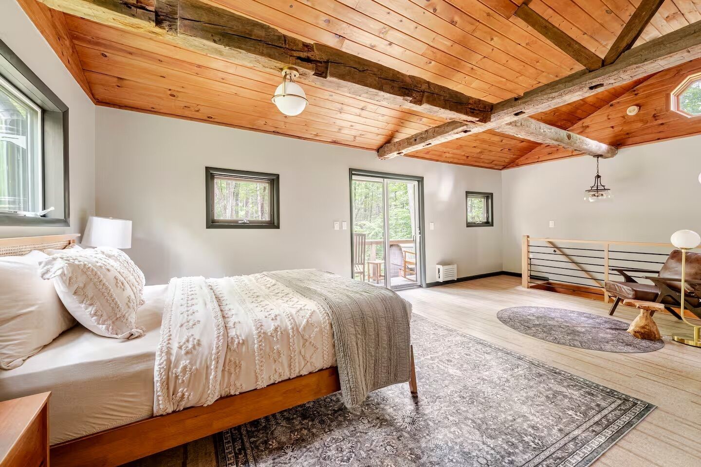 Une chambre avec un plafond en bois, un lit recouvert d’une couverture blanche et grise, une fenêtre et une vue sur l’extérieur.