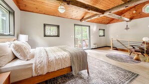 Ein Schlafzimmer mit Holzboden, einem Bett mit weißer und grauer Decke, einem Fenster und Blick ins Freie.