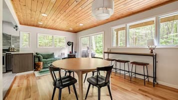 Une cuisine moderne avec un plafond en bois, de grandes fenêtres et une table à manger ronde entourée de chaises.