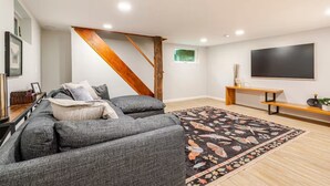 Ein modernes Wohnzimmer mit einer Couch, einer hölzernen Bank, einem Flachbildfernseher und einem gemusterten Teppich.