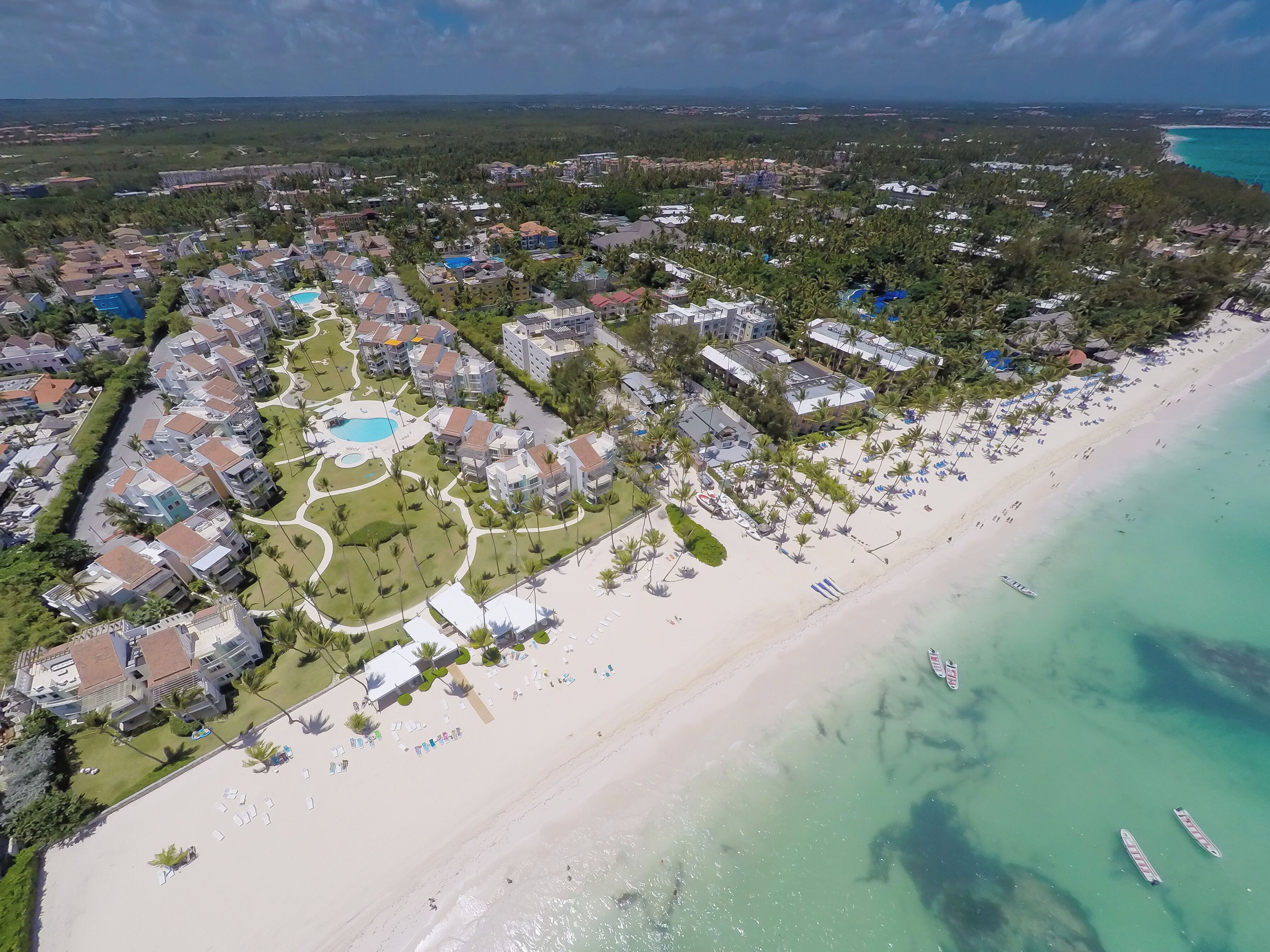 An aerial view of a coastal resort with multiple buildings, a beach, and clear turquoise waters.
