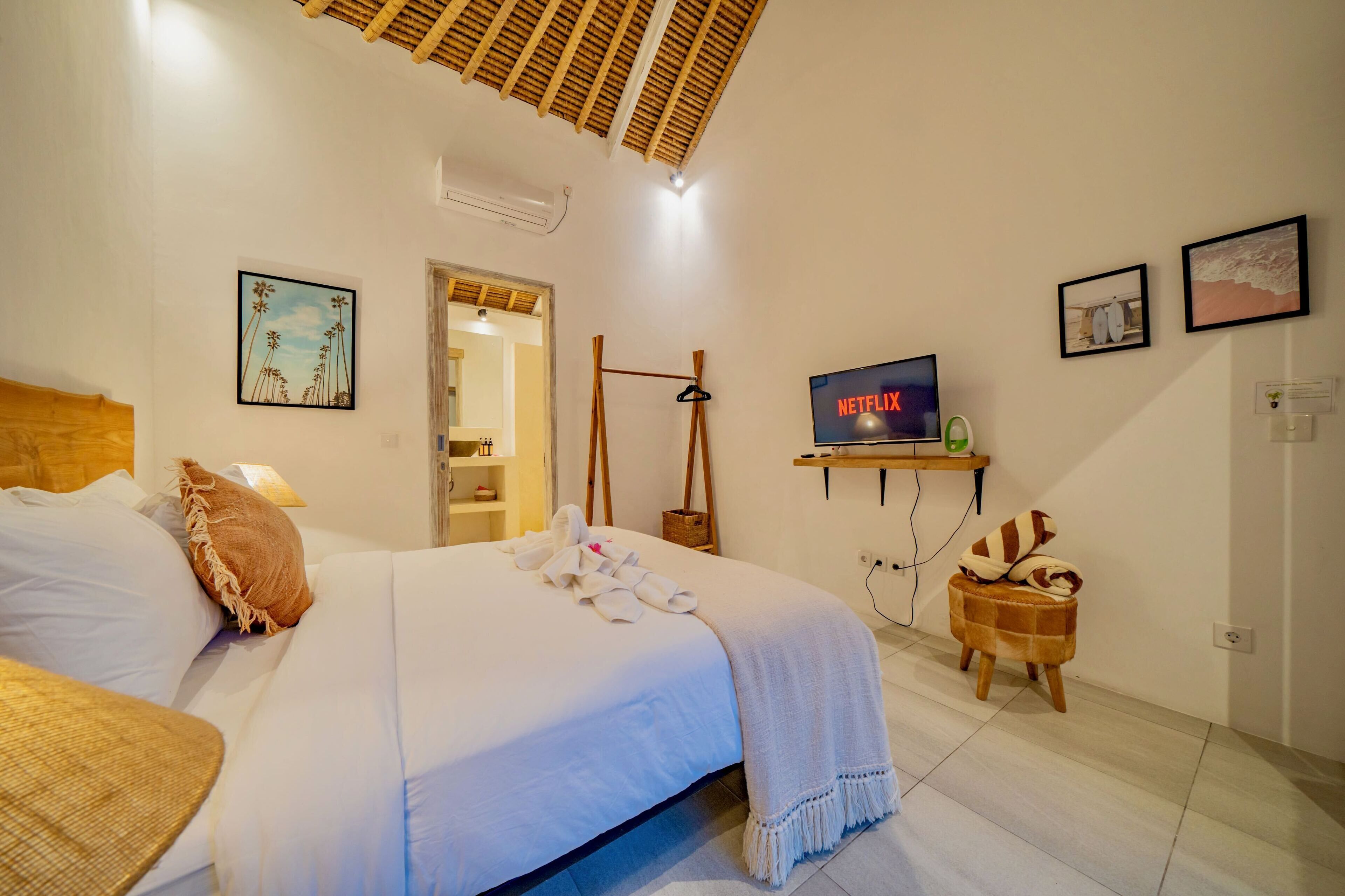 Una habitación de hotel con una cama, un televisor, una estantería con el logo de Netflix y obras de arte en las paredes.