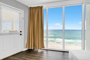 A room with a large window overlooking a beach, a door with blinds, and a bed. - ☀️Beachfront Views-Multiple Pools-Long Beach Resort 2-1304☀️ (Panama City Beach)