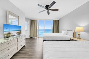 A hotel room with a large window, a ceiling fan, a TV, a bed, a dresser, and a lamp. - ☀️Beachfront Views-Multiple Pools-Long Beach Resort 2-1304☀️ (Panama City Beach)