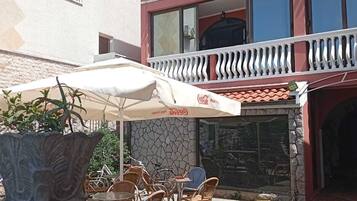 A building with a two-story balcony, outdoor seating with umbrellas, and a Coca-Cola sign.