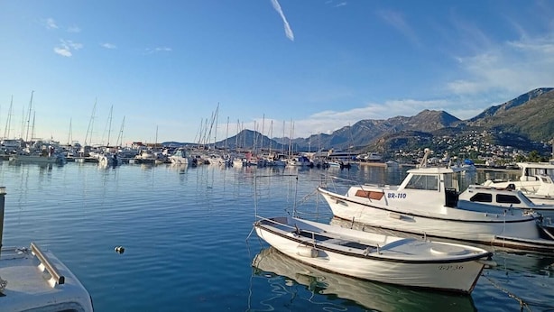 Un port de plaisance avec des bateaux amarrés, une eau calme et un paysage montagneux en arrière-plan.