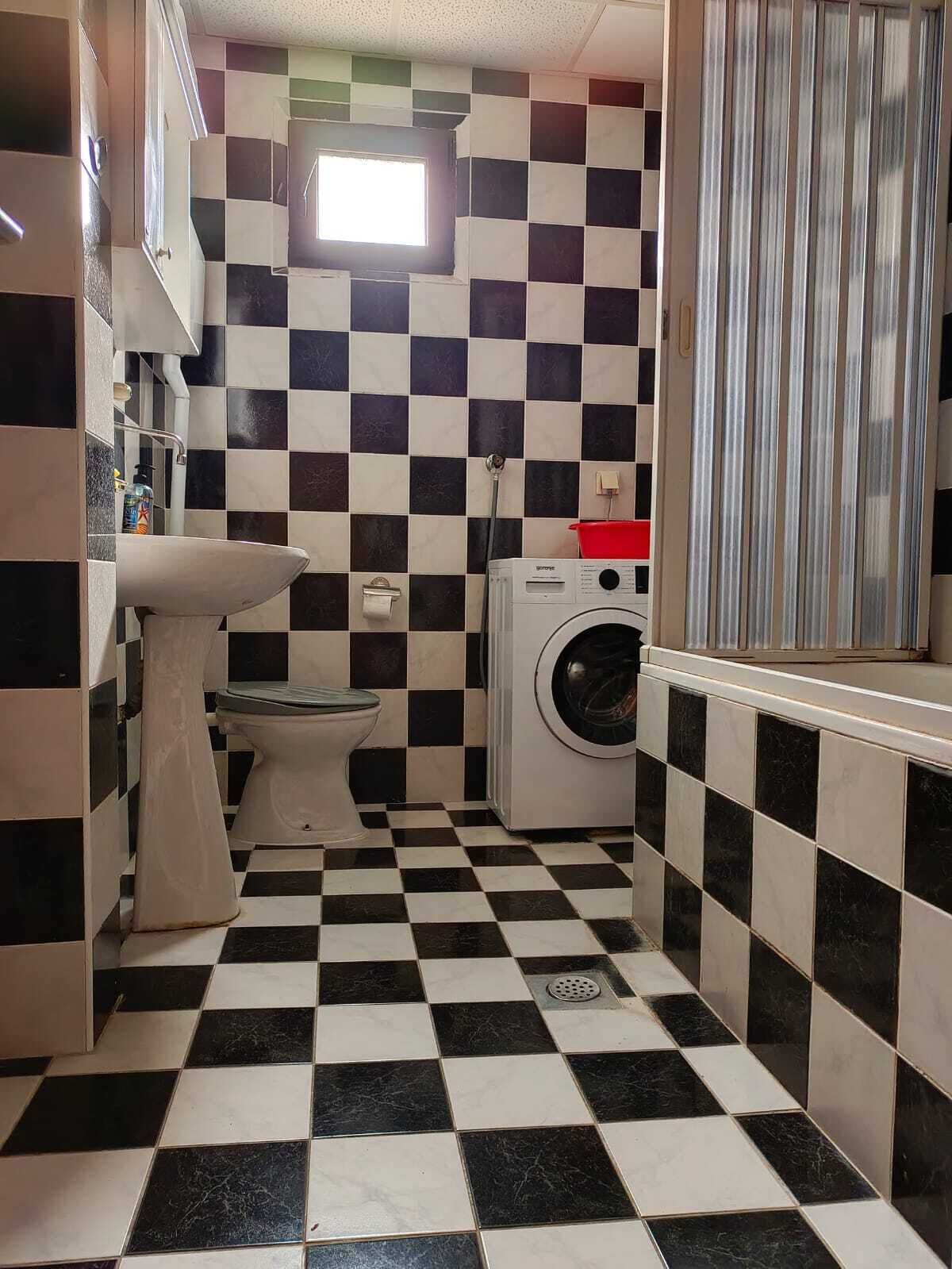 A small bathroom with a checkered floor, a sink, a toilet, and a washing machine.