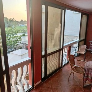 A balcony with a view of a road and greenery, a white railing, and wicker chairs. - Apartmani Kolovic Susanj (Bar)