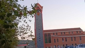 Un bâtiment doté d’une haute tour, un parking rempli de voitures et une zone herbeuse.