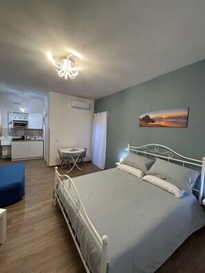 A bedroom with a bed, a desk, a chair, and a kitchenette in the background. - Maison Laezza (Naples)