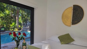 A bedroom with a bed, a view of a pool, and a decorative wall piece.