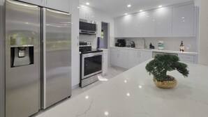 A modern kitchen with stainless steel appliances, white cabinetry, and a marble countertop.