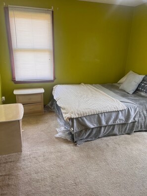 Une chambre à coucher avec un lit, une table de chevet, une fenêtre avec des stores et un mur vert.