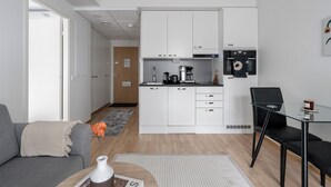 Eine moderne Küche mit weißen Schränken, einer Kaffeemaschine und einer Mikrowelle. Es gibt eine Essecke mit einem Glastisch und schwarzen Stühlen.